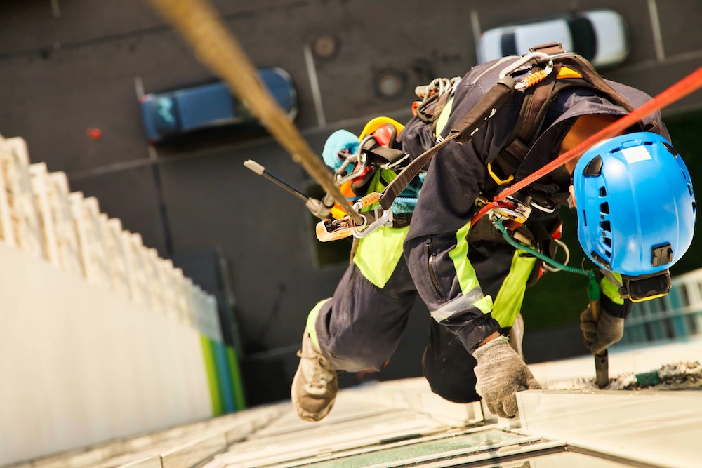 Industriell bergsklättringsarbetare hänger över bostadsfasadbyggnad under städarbete för höghus